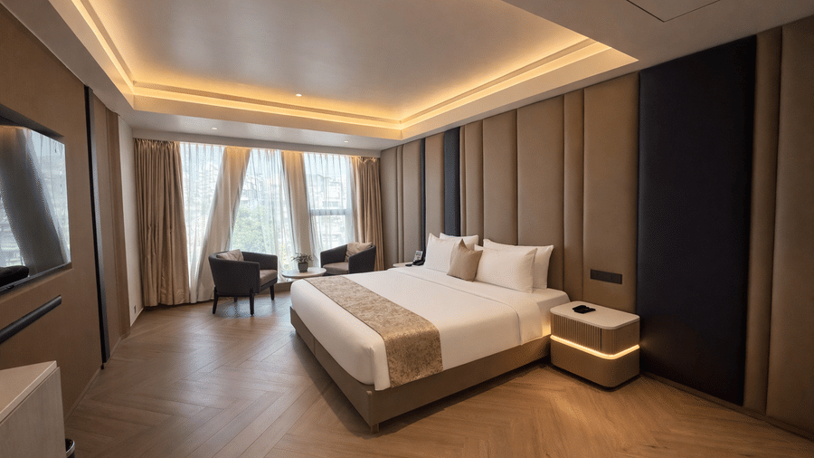 Premium room at Dragonfly Hotel – The Art Hotel with large bed, white linens, beige and brown accent pillows, wall paneling, pendant lights, seating area near window, and warm recessed lighting.