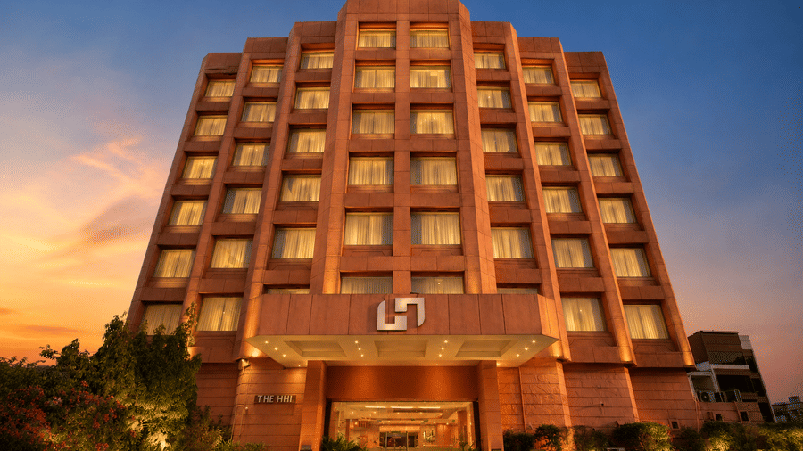 Grand hotel facade at twilight with golden-lit windows, ornate entrance, and landscaped grounds.