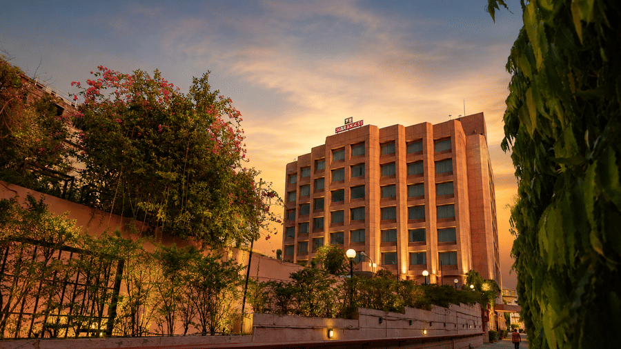 Hotel exterior at golden sunset with bougainvillea, lush greenery, and warm facade lighting.