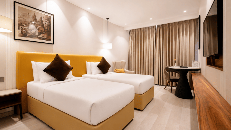 The Deluxe Room interior at HHI Varanasi featuring a king size bed, wooden accents, and warm ambient lighting.