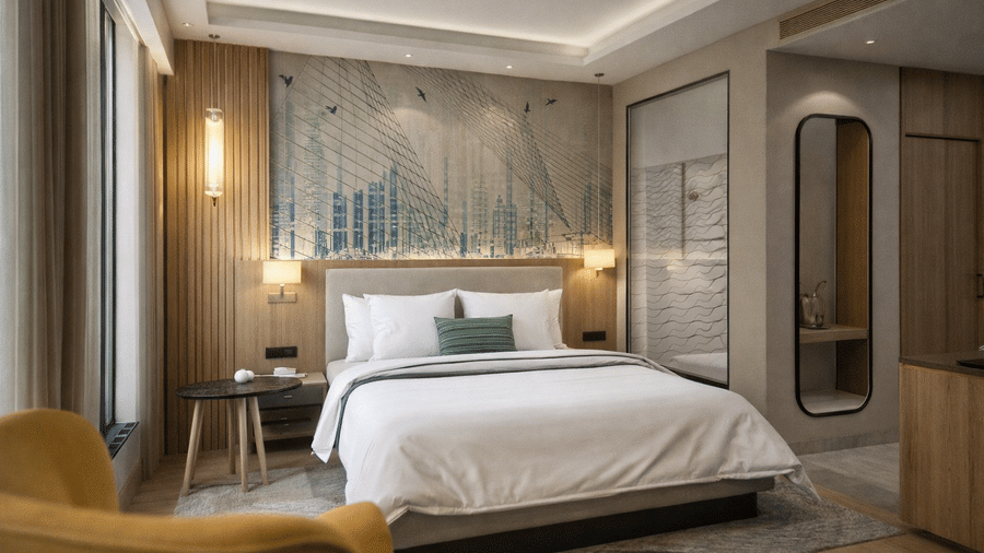 A modern bedroom at KPG Sarovar Portico, Raj Nagar Extension, Ghaziabad, featuring a king size bed, an upholstered armchair, and a decorative textured wall panel behind the headboard.