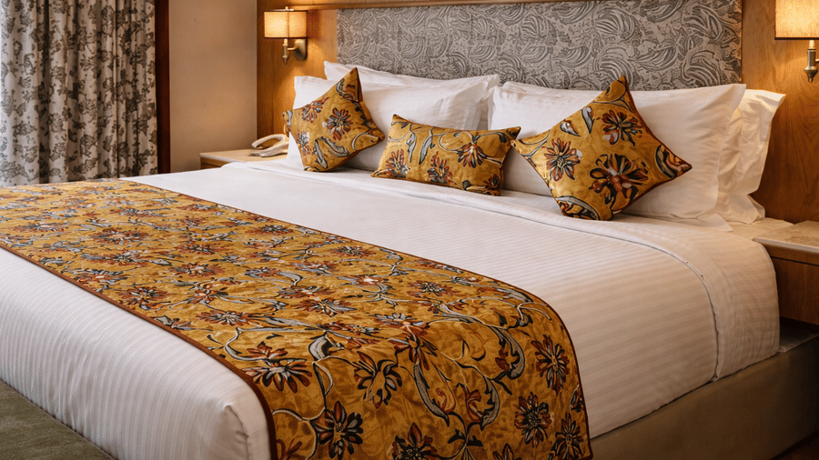 A room at Mountnoor Sarovar Premiere, dressed in crisp linens and accented with a decorative patterned bed runner and matching throw pillows against a padded headboard.