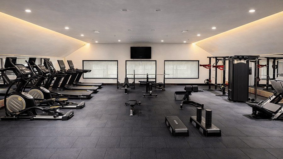 Side view of the indoor gym at Mountnoor Sarovar Premiere, Pahalgam, equipped with cycling machines, treadmills, and place settings for body training.