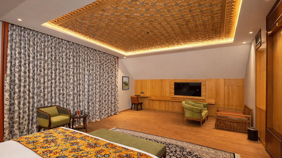 An upscale Junior Suite at Mountnoor Sarovar Premiere featuring patterned curtains, a king size bed, and a decorative textured ceiling with warm lighting.