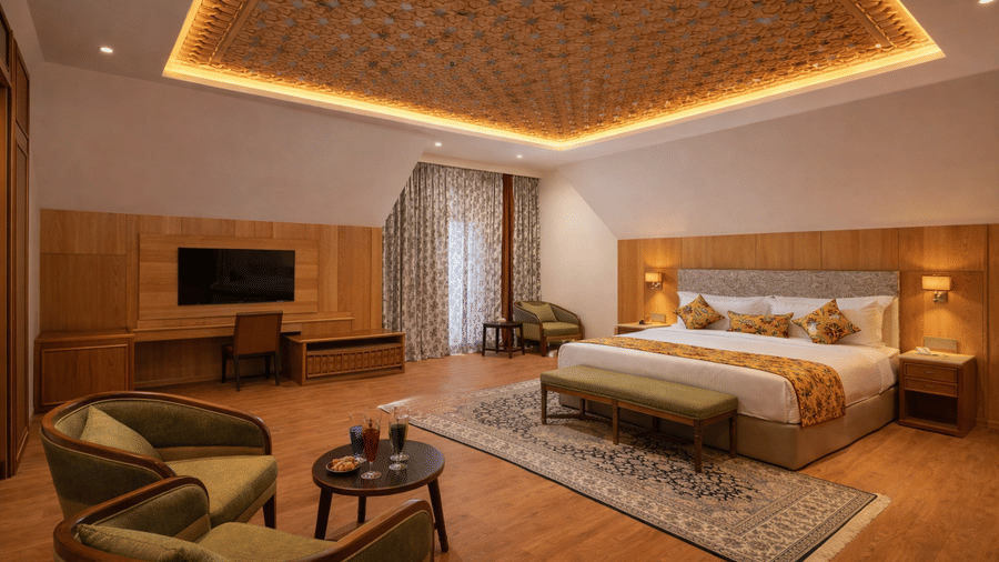 A Junior Suite at Mountnoor Sarovar Premiere featuring a sleeping area with a king size bed, a lounge area with 2 chairs, and a wall-mounted television.