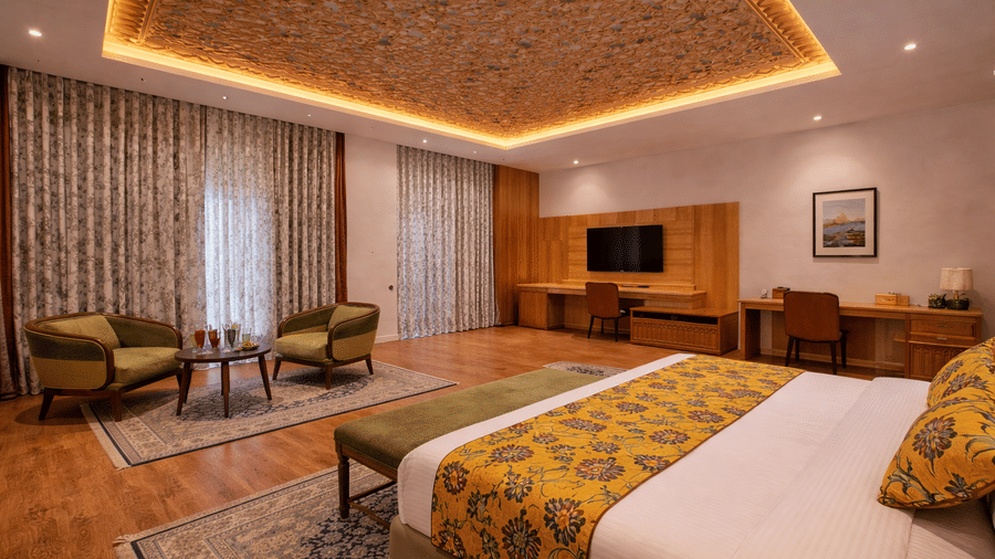A premium guest suite at Mountnoor Sarovar Premiere featuring a king size bed, a wooden desk area, and 2 armchairs set around a small coffee table.