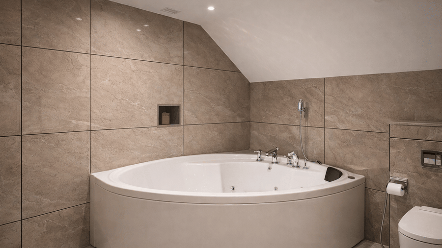 A modern bathroom in a Junior Suite at Mountnoor Sarovar Premiere featuring a large corner bathtub and large wall tiles under recessed ceiling lights.