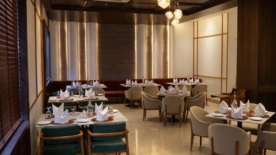 A dining space at Mountnoor Sarovar Premiere, Pahalgam, with designed with paneled walls, decorative lighting fixtures, and dark ceiling beams.