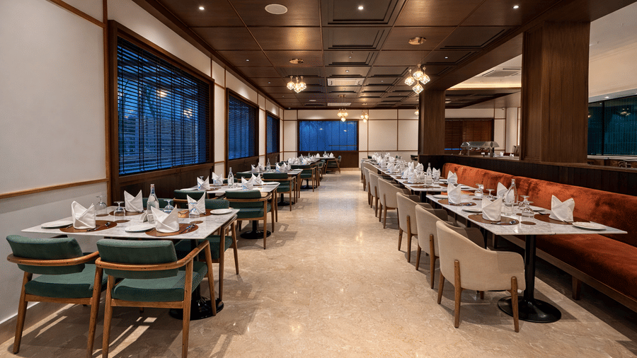 Wide angle view of Noor All-day Dining at Mountnoor Sarovar Premiere, Pahalgam, with neatly arranged tables and large glass windows offering views of the surroundings.