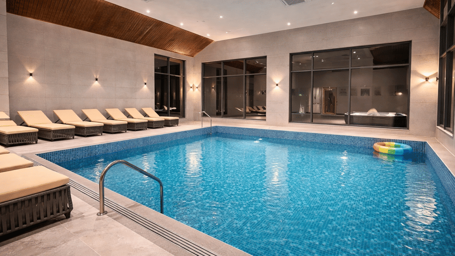 Indoor pool of Mountnoor Sarovar Premiere, Pahalgam, seen with clean water, a floatie in it, and lounge chairs placed on the pool deck.