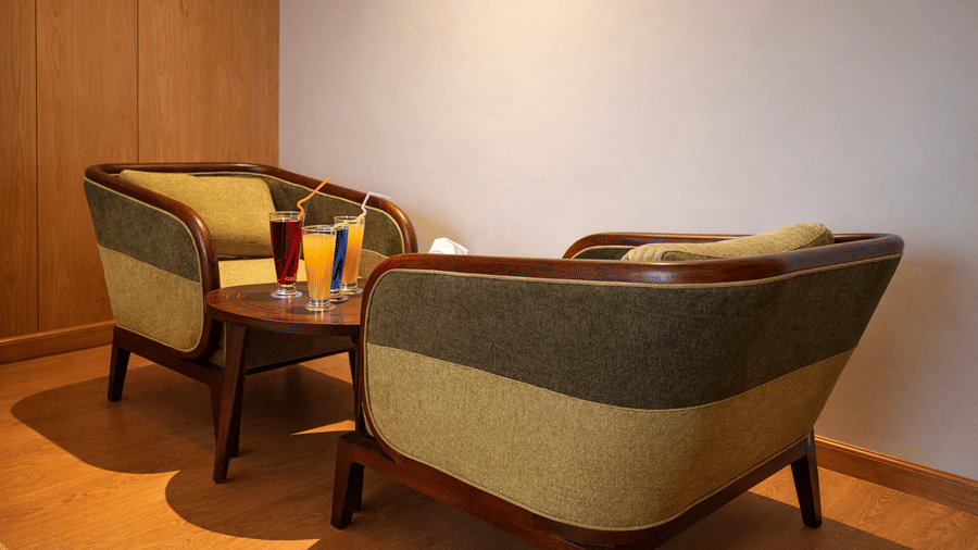 A close-up of a seating area in a Mountnoor Sarovar Premiere room, with 2 upholstered armchairs and a wooden table holding 2 tall glasses.