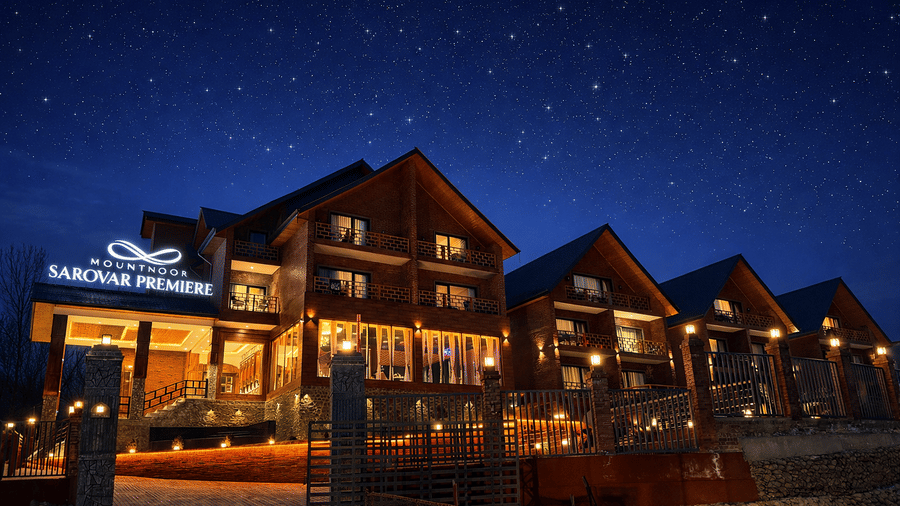 Facade of Mountnoor Sarovar Premiere, Pahalgam, seen with brightly lit signage and interiors, during the night under the dark sky full of stars.