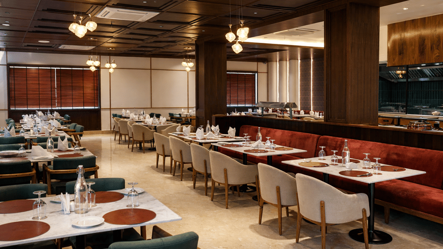 Interior of Noor All-day Dining at Mountnoor Sarovar Premiere, Pahalgam, featuring neatly arranged dining tables with place settings, and ambient overhead lighting.