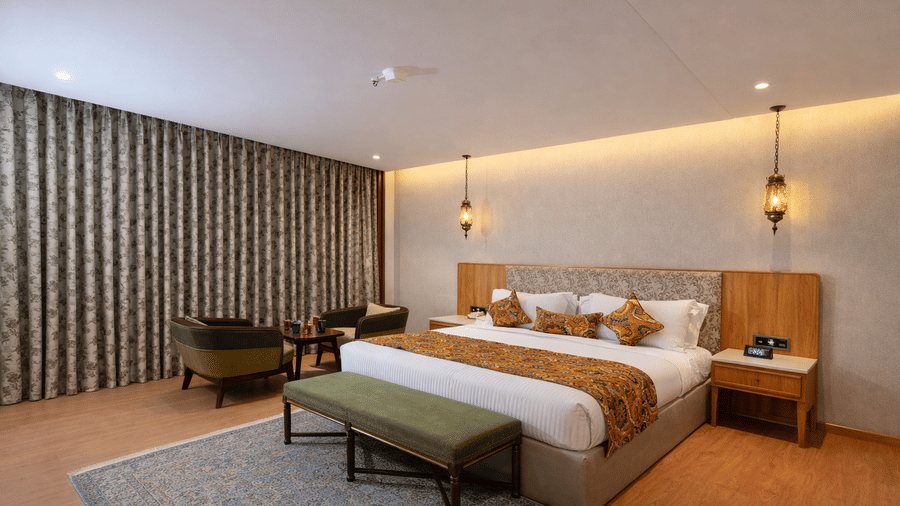 Bedroom of Superior Room with Bathtub furnished with a king size bed, a bench on a carpet, bedside tables, a seating area for 2, and 2 lights hung near the wall from the ceiling.