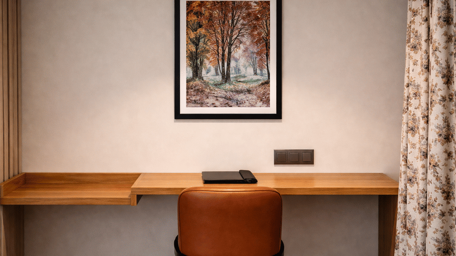 Work desk in the Superior Room with Bathtub featuring a wooden desk attached to the wall, and an upholstered chair placed facing it. An art piece is hung on the wall as well | Mountnoor Sarovar Premiere, Pahalgam