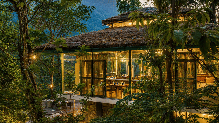 Warmly-lit Glasshouse restaurant nestled amidst lush trees at Neemrana's Glasshouse on The Ganges - 21st Century, Rishikesh.