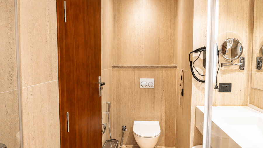 A toilet area in the ensuite bathroom of a Premium Room at Pride Plaza Indore, showing a wall-hung toilet, a wooden door, and a vanity counter.