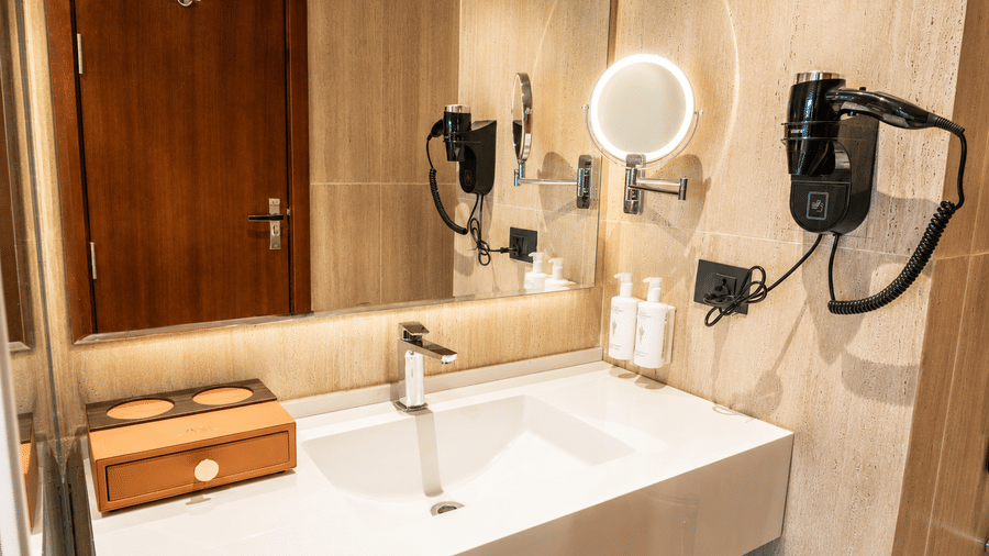An ensuite bathroom in the Superior Twin Room at Pride Plaza Indore featuring a washbasin, mirror with integrated light, and wall hairdryer.