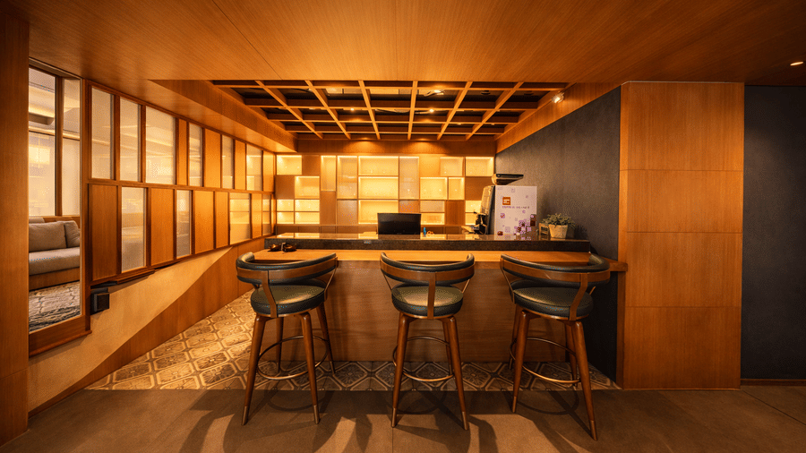 A bar counter with high stools facing shelves and wooden wall panels | Pride Premier Darjeeling