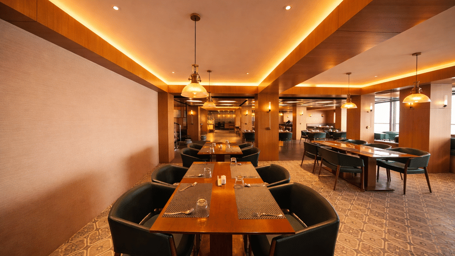 A dining room with rectangular tables, chairs, and illuminated ceiling panels | Pride Premier Darjeeling