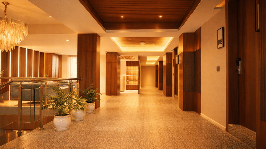 A brightly lit hotel corridor with wooden wall panels and potted plants | Pride Premier Darjeeling