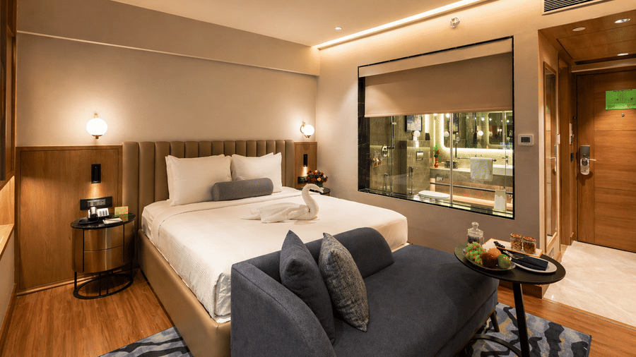 Bedroom at Pride Premier Pune with a king size bed, sofa seating and a glass partition to the bathroom.