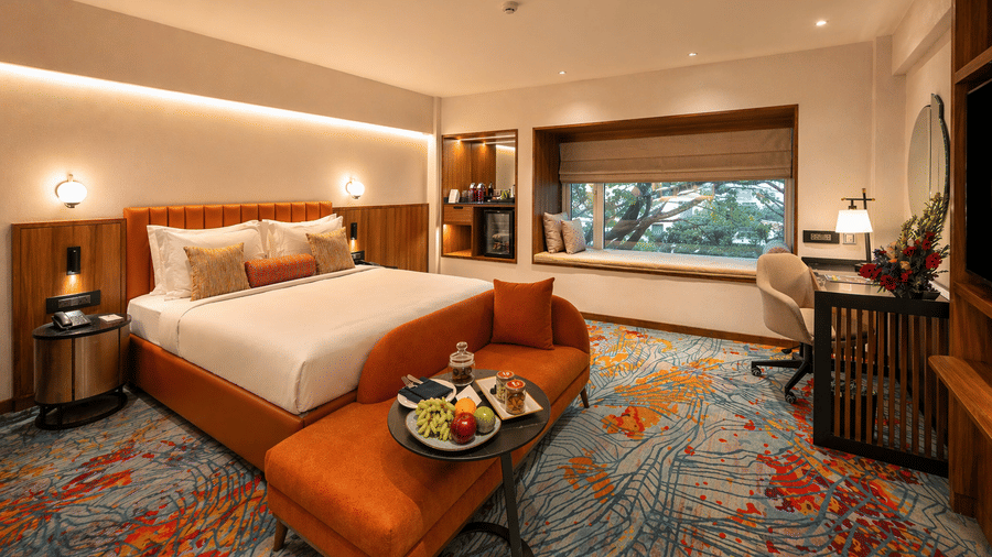 Elegant bedroom at Pride Premier Pune with a king size bed, cushioned bench and fruit platter on the table.