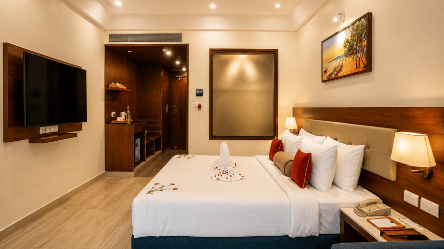 Deluxe King Room with Balcony at Sobit Sarovar Portico, Goa featuring a king size bed, cosy seating area, private balcony overlooking lush greenery, work desk, modern amenities and stylish interiors.