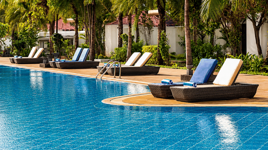 Swimming pool with wooden lounge chairs and blue cushions surrounded by palm trees at Chariot Beach Resort, perfect for relaxing days.