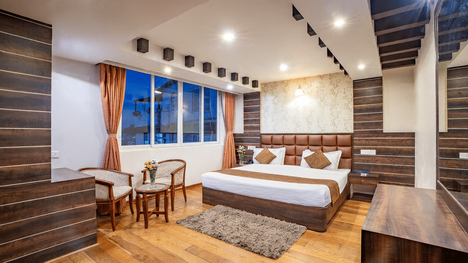 A comfortable hotel room with a large bed, seating area, and a view of the city at the Yashshree Jai Hotel & Banquet, Darjeeling.