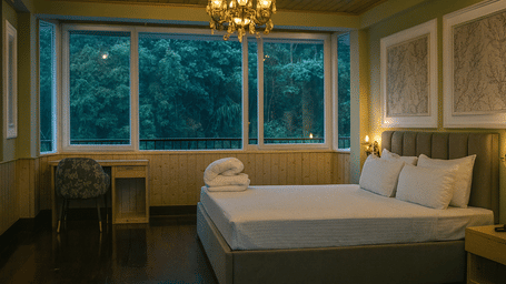 Luxury hotel room in Kurseong with chandelier, elegant bed, wooden interiors, and large windows overlooking lush green forest view
