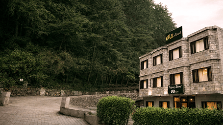 Exterior view of DLS La Serene Valley, Manali, showing a multi-story building with illuminated windows, private balconies, and ground-level parking spaces containing parked vehicles under a dark night sky.