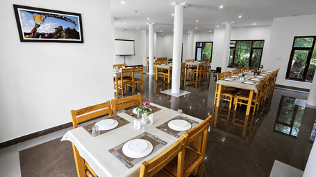 A dining space with tables, chairs, plates, and wall arts at Indus Serinity, Leh Ladakh.