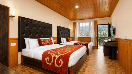 Two beds are placed in the Family Room at Orsino Khangri Karpo Retreat & Spa, Lachung. Timber panels cover the ceiling and the lower half of the walls. A window and a television stand in the corner.