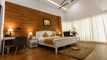Room at Polo Resort Cherrapunji with white wooden bed, mustard runner, desk, lamps, wood flooring and floral arrangement.