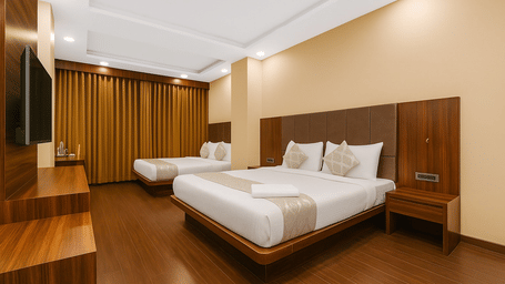 A spacious hotel room featuring two large beds with white linens, wooden flooring, and warm wood wall paneling.