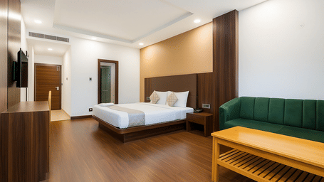 A hotel room featuring a large bed and a green upholstered sofa with a light wood coffee table.