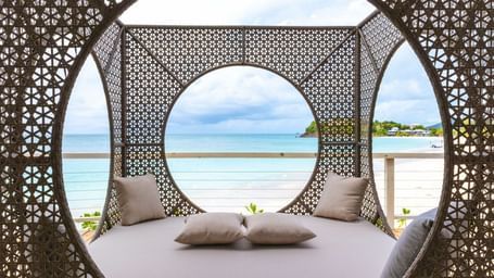 A decorative, circular outdoor daybed with intricate patterns offers a view of a serene beach and ocean.