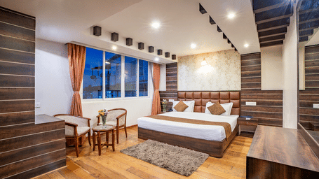 A comfortable hotel room with a large bed, seating area, and a view of the city at the Yashshree Jai Hotel & Banquet, Darjeeling.