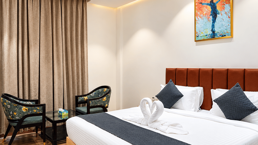 Bed with towel art, black cushions, and two armchairs beside curtains at Daksh The Royal Braj, Vrindavan.