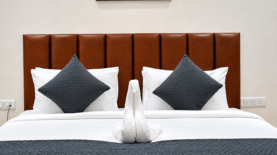 Close view of a bed with a brown headboard, black cushions, towel art, and a black runner at Daksh The Royal Braj, Vrindavan.