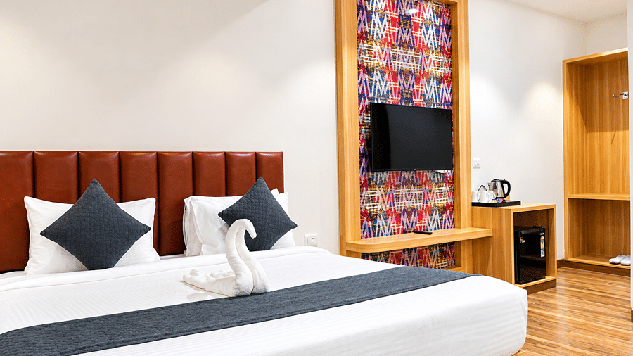 Bed with a black runner and towel art in front of a wall-mounted television and wooden panelling at Daksh The Royal Braj, Vrindavan.