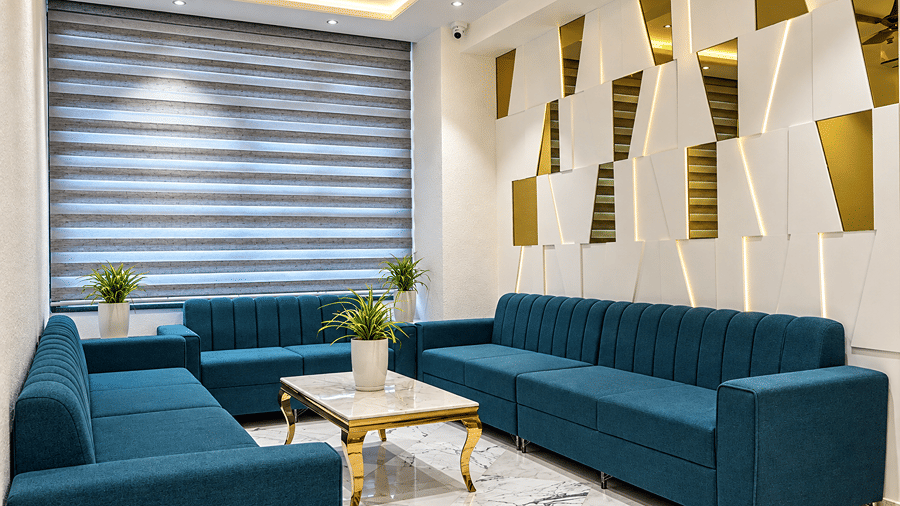 Blue sofas with a coffee table beside window blinds and golden wall panels at Daksh The Royal Braj, Vrindavan.