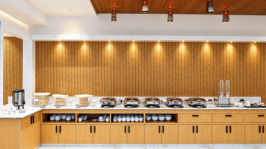 Buffet counter with chafing dishes against a wooden panelled wall at Daksh The Royal Braj, Vrindavan.