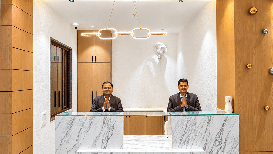 Front desk at Daksh The Royal Braj, Vrindavan, with two staff members behind a marble-based counter and wooden wall panelling.