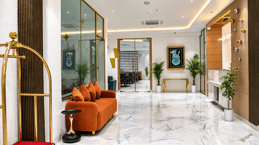 Lobby at Daksh The Royal Braj, Vrindavan, with an orange sofa, a luggage trolley, and a marble floor leading to glass doors.