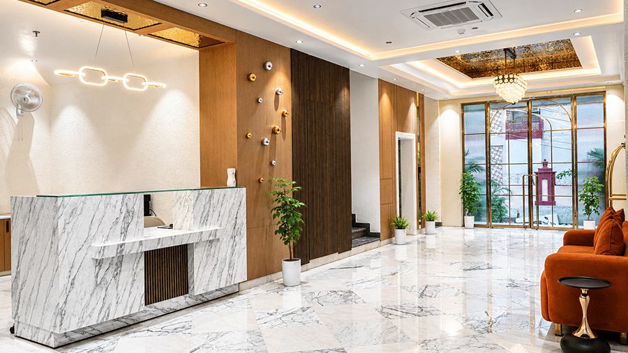 Lobby of Daksh The Royal Braj, Vrindavan, featuring a marble reception counter, wooden panelling, and a marble floor with an orange chair.