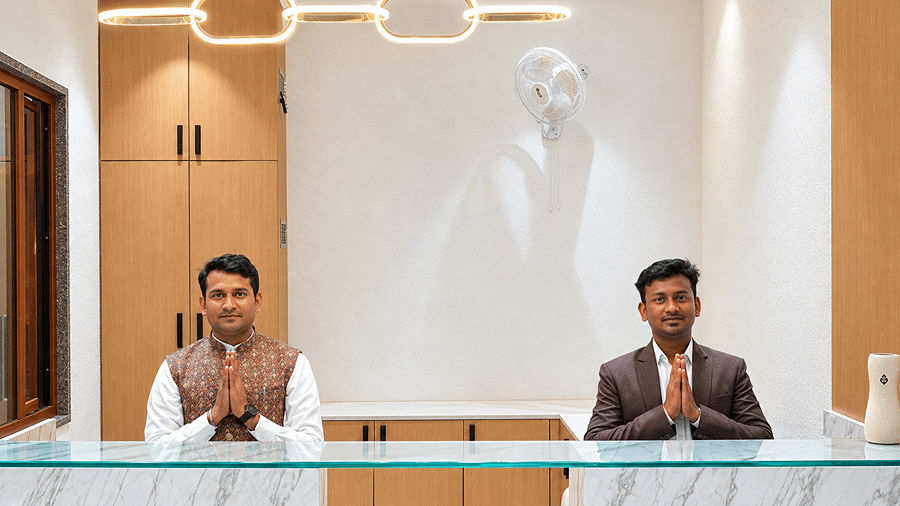 Two staff members with folded hands behind the glass-topped reception desk at Daksh The Royal Braj, Vrindavan.