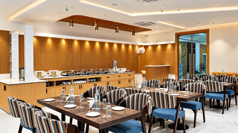 Restaurant at Daksh The Royal Braj, Vrindavan, with a buffet counter at the back and dining tables with striped chairs in the foreground.