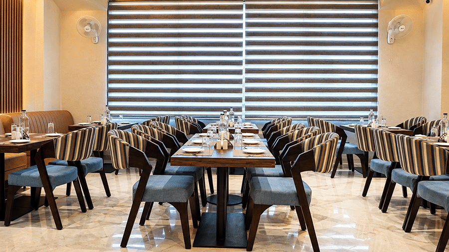 Restaurant at Daksh The Royal Braj, Vrindavan, with dining tables, striped chairs, and window blinds.